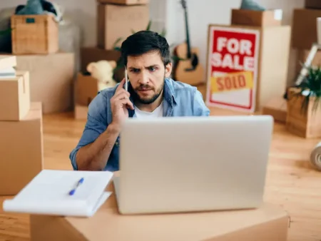 How Do You Prepare for a Last-Minute Move in Chicago? A 2025 Survival Guide Man talks on the phone while checking a laptop among moving boxes and a sold home sign